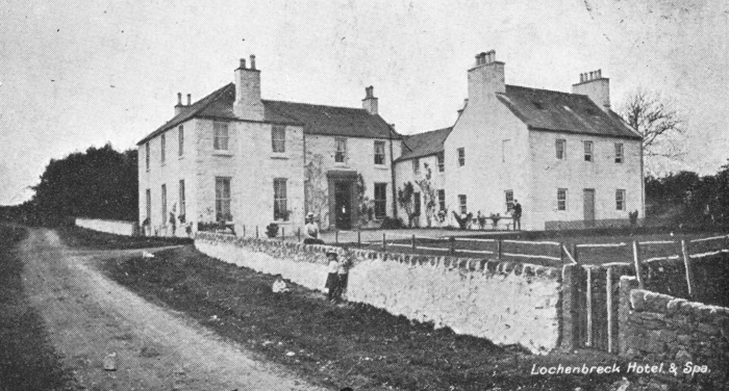 black and white photo of a massive house and 2 children stood near a wall
